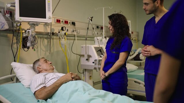 Slow-motion shot of a smiling doctor attending sick male patient and consulting him in hospital ward