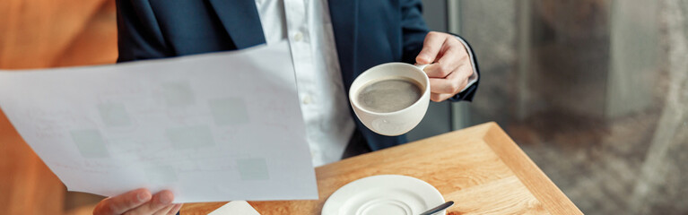 Close up of unrecognisable businessman drinking coffee and working with documents in cafe