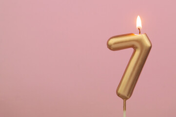Burning gold birthday candle on pink background, number 7. Large copy space for text.