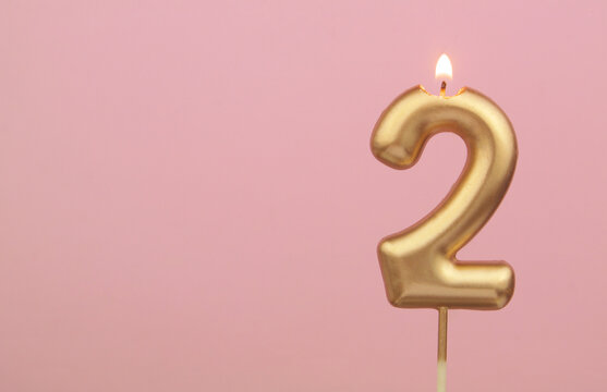 Burning gold birthday candle on pink background, number 2. Large copy space for text.
