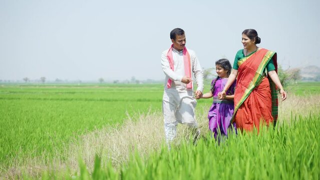 Happy village couple with kid walking by talking each other near paddy field - concept of sustainable lifestyle, family bonding and rural India.