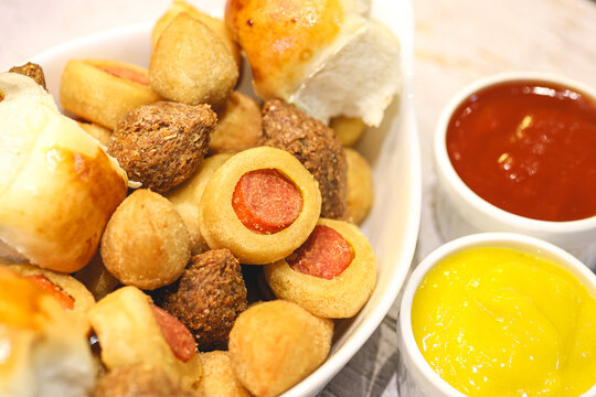 Salgados brasileiros variados dentro de uma assadeira e potes com ketchup e mostarda ao lado. Comida brasileira, lanche, aperitivo, salgadinho.