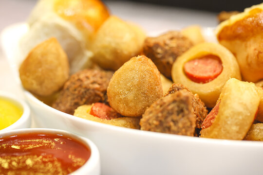 Salgados brasileiros variados dentro de uma assadeira sobre uma mesa de madeira. Potes com Ketchup e mostarda na composi&ccedil;&atilde;o. Comida brasileira, lanche, aperitivo, salgadinho, petisco brasileiro.	
