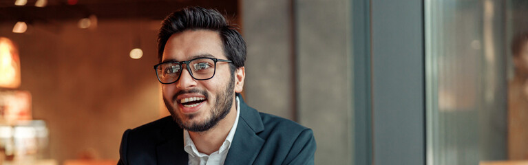 Smiling businessman working with graphs and charts at modern cafe and looking at side