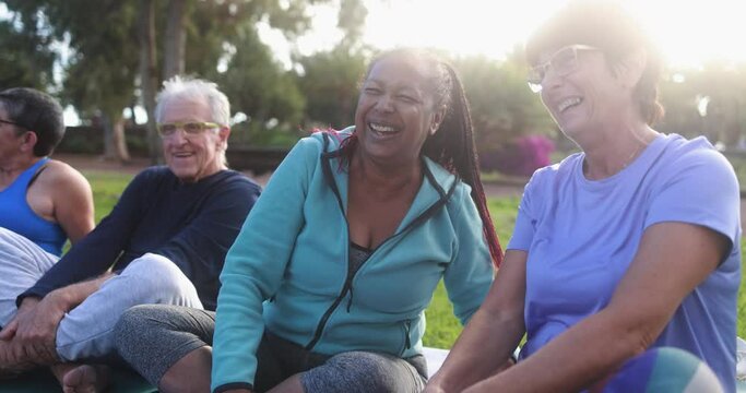 Multiracial senior people having fun after workout exercises outdoor with city park in background - Healthy lifestyle and joyful elderly lifestyle concept