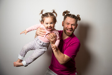 Young caucasian bearded father in bright pink t-shirt with two tails having fun with his little smiling daughter with two tails