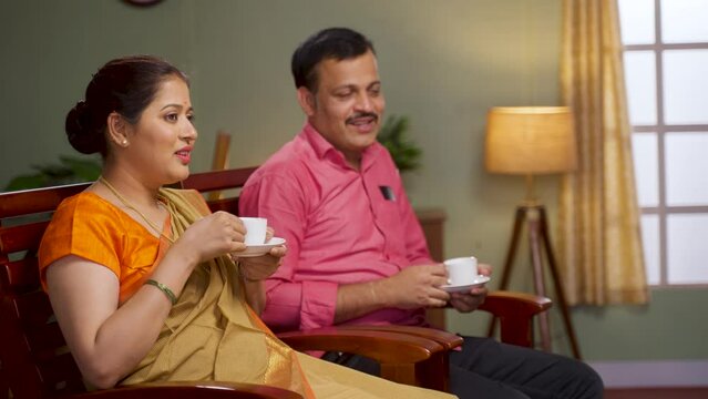 relxed couple having tea while watching tv or television at home by talking each other - concept of refreshment, healthy lifestyle and family relationship