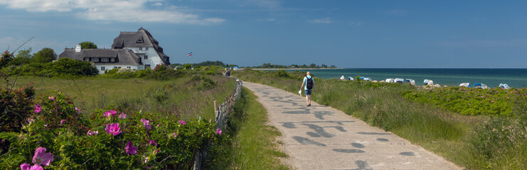 Back view of a vacationer walking along a scenic coastal path at Hohwacht beach in summer.