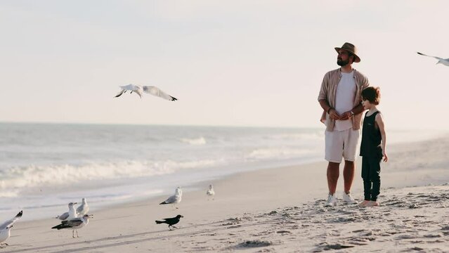 father and son feeding seaguls at the ocean shore. family having fun together