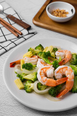 Fried broccoli and shrimp with oyster sauce, onion and corn in white dish on concrete table.