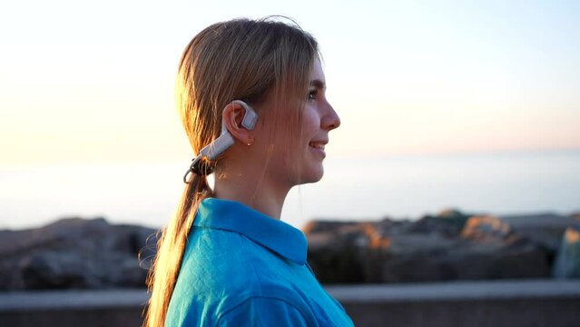 young female walking in bone conduction headphones in sunset