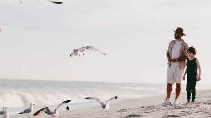 cheerful family spending time together on the sandy beach, playing in sand, feeding birds