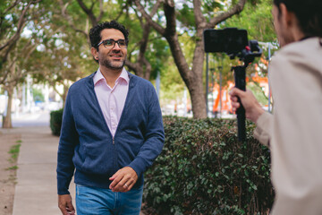 Middle-aged man walking confidently and smiling while being filmed with a cell phone on a gimbal.