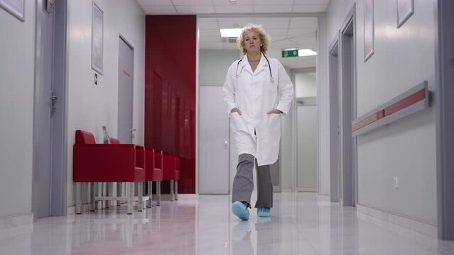 Female doctor uses mobile phone while walking in shoe cover through hospital hallway in slow-motion