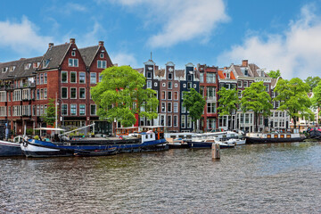 Fototapeta na wymiar Typical houses with colorful facades in Amsterdam and cruise boats. The Amstel River.