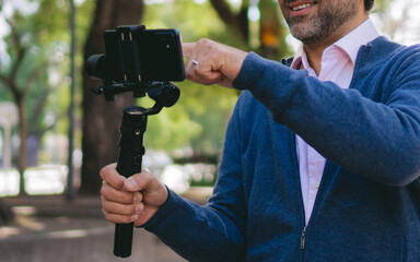 Middle-aged Latin man holding his cell phone with a gimbal while interacting with it.