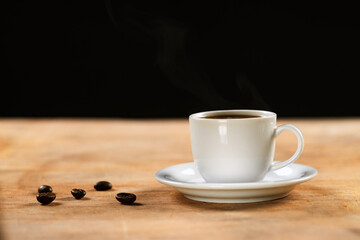 Coffee cup and coffee beans on wooden table. Black background.