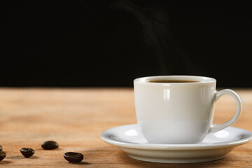 Coffee cup and coffee beans on wooden table. Black background.