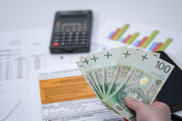 polskie banknoty trzymane w dłoni na tle formularzy, tabelek i wykresów i kalkulatora - obrazy, fototapety, plakaty