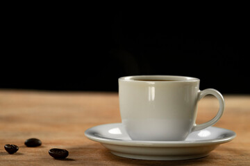 Coffee cup and coffee beans on wooden table. Black background.