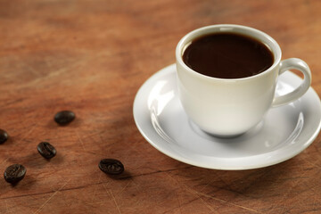 Coffee cup and coffee beans on wooden table. Black background.