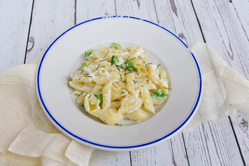 Plate of pasta with cream cheese and herbs. Cheese sauce pasta served on wooden table 