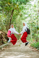 two female elementary students in uniform jumping happily at the country road with hand in hand