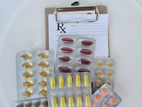 Pile of different pills and paper list of prescription closeup