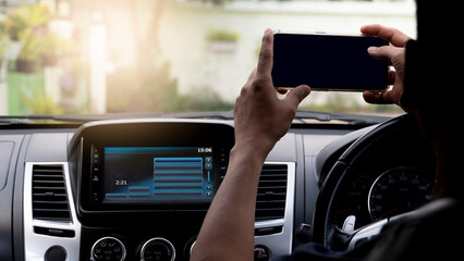 Hand of driving man hold and touch mobile phone for take photo or something. Console cars in the center open multimedia display. and blurred background of th city.