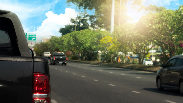 Back side of pick up car bleck color on the asphalt road. Clear streets with few cars. Beside road with trees. and background under of blue sky and white clouds.