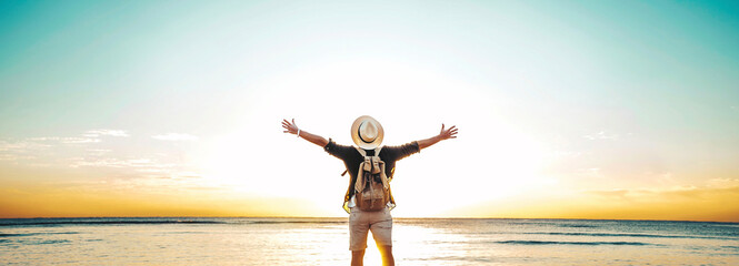Back view of happy excited man raising arms up to blue sky - Hipster winner traveler enjoying summer sunset at the beach - Travel, mental health, success, business, tourism and life style concept