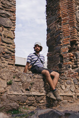 Low angle view of a young latin man with a bucket hat sitting in an antique window frame. Vertical photo.