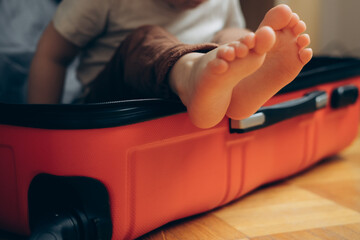 travel concept. The child is sitting in a suitcase at the home, child's bare foot