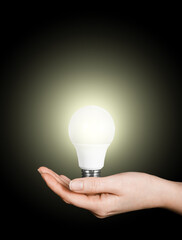 woman's hand holding led light bulb on black background, energy concept, war in Ukraine, blackout, Electricity problems