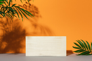 Wooden cube podium on orange background with shadows of palm leaves. Product display, scene stage...