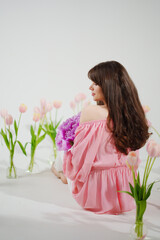 beautiful brunette woman with long hair sits on the floor with vases of flowers 