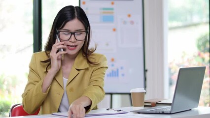 A businesswoman on the phone calling a client is reading some documents on her desk in the office. Woman talking on the phone to someone while analyzing documents and reading monthly work schedule.