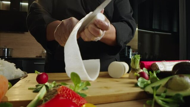 Professional male chef in hand gloves slicing fresh japanese daikon with a sharp knife in kitchen close-up. Process of preparing delicious rolling sushi in slow-motion