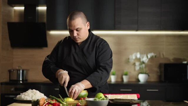 Slow-motion shot ofa man's hands cutting and slicing mango on cutting wooden board of home in kitchen. Man preparing ingredients for making sushi