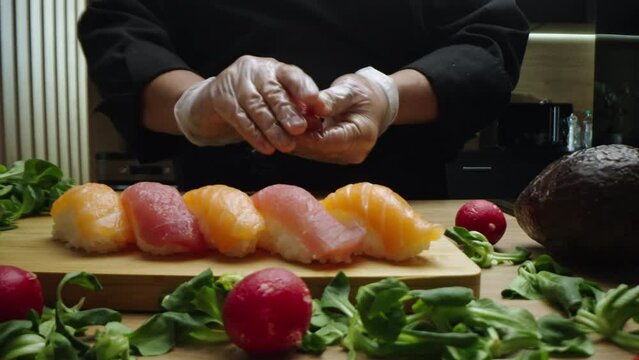 Slow-motion shot of a young man making salmon nigiri sushi in the kitchen and arranging them on wooden boad