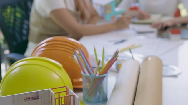 Tilt up shot of scale model house on table with helmets and two female architects discussing work issues. interior designer discussing a house plan on a blueprint. Architect contractor meetings.