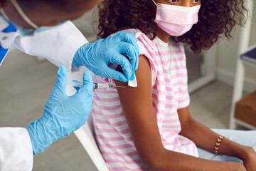 African American teenage girl receives flu shot from her family doctor at hospital. Close-up of...