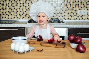 Little girl cooking in the kitchen wearing an apron and a chef's hat.