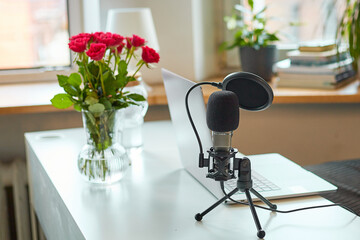 Laptop on a white table, rose flowers in a vase and a desktop microphone nearby.