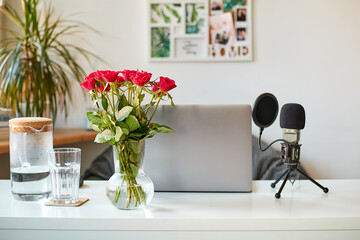 Laptop on a white table, rose flowers in a vase and a desktop microphone nearby.