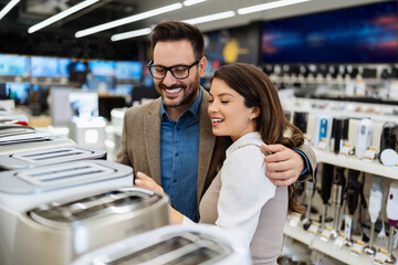 Beautiful and happy middle age couple buying consumer tech products in modern home tech store. They...