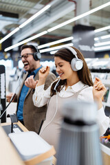 Beautiful and happy middle age couple buying consumer tech products in modern home electronics store. They are choosing high quality hifi audio speakers and audiophiles headphones.