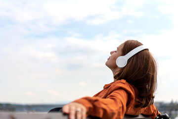 Fototapeta na wymiar Woman sitting on bench outdoors listening music using wireless headphones.