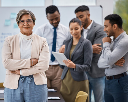 Leading her team towards greatness. Portrait of a mature businesswoman standing with her arms crossed in an office with her colleagues in the background.