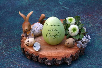 Grußkarte Frohe Ostern: Osterhase mit einem beschrifteten Osterei auf einer Baumscheibe dekoriert....